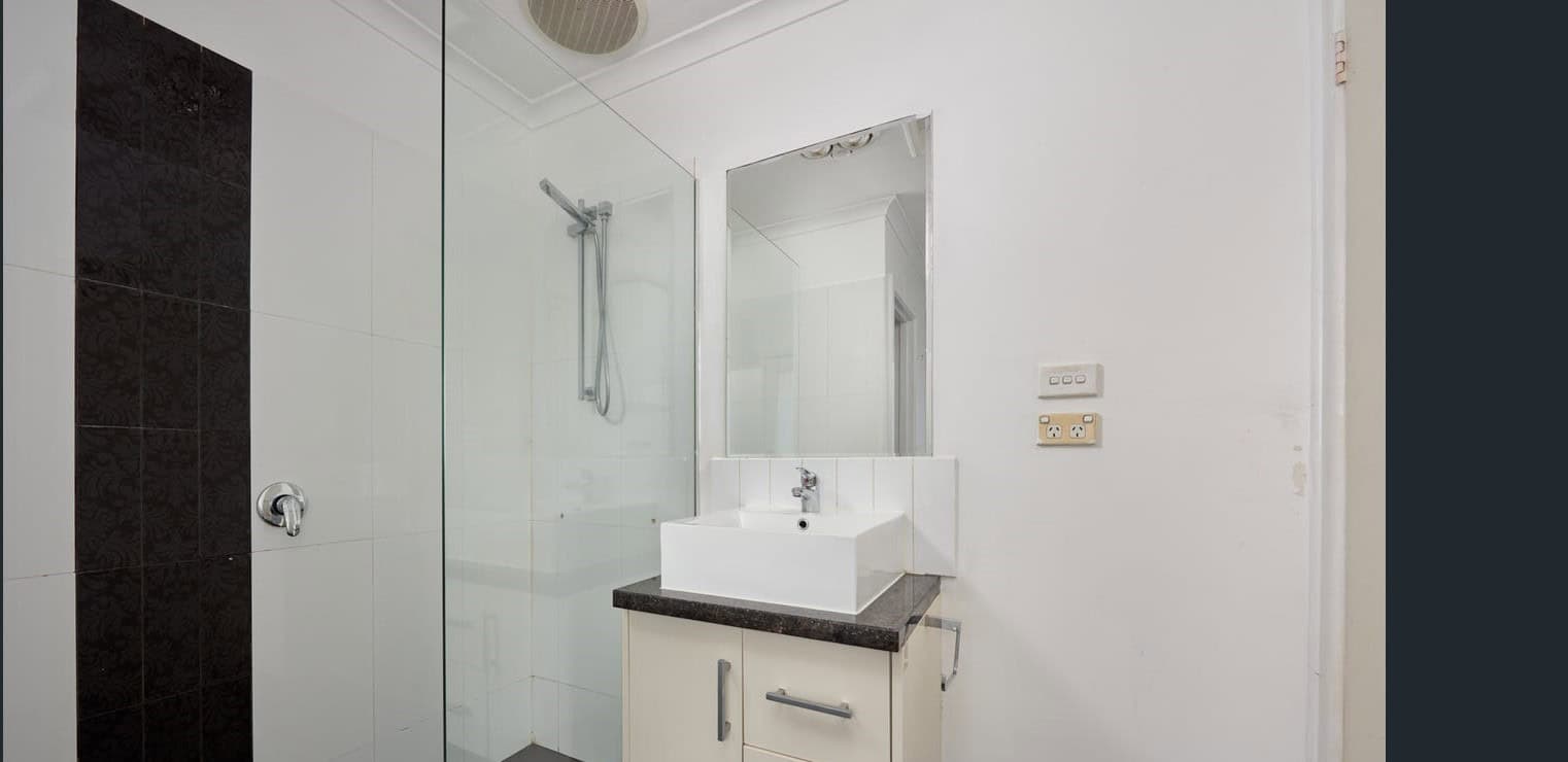 Bright modern bathroom featuring a sleek shower, white vanity with black countertop, large mirror, and contemporary fixtures — ideal for property listings at Ember Estate Agents.
