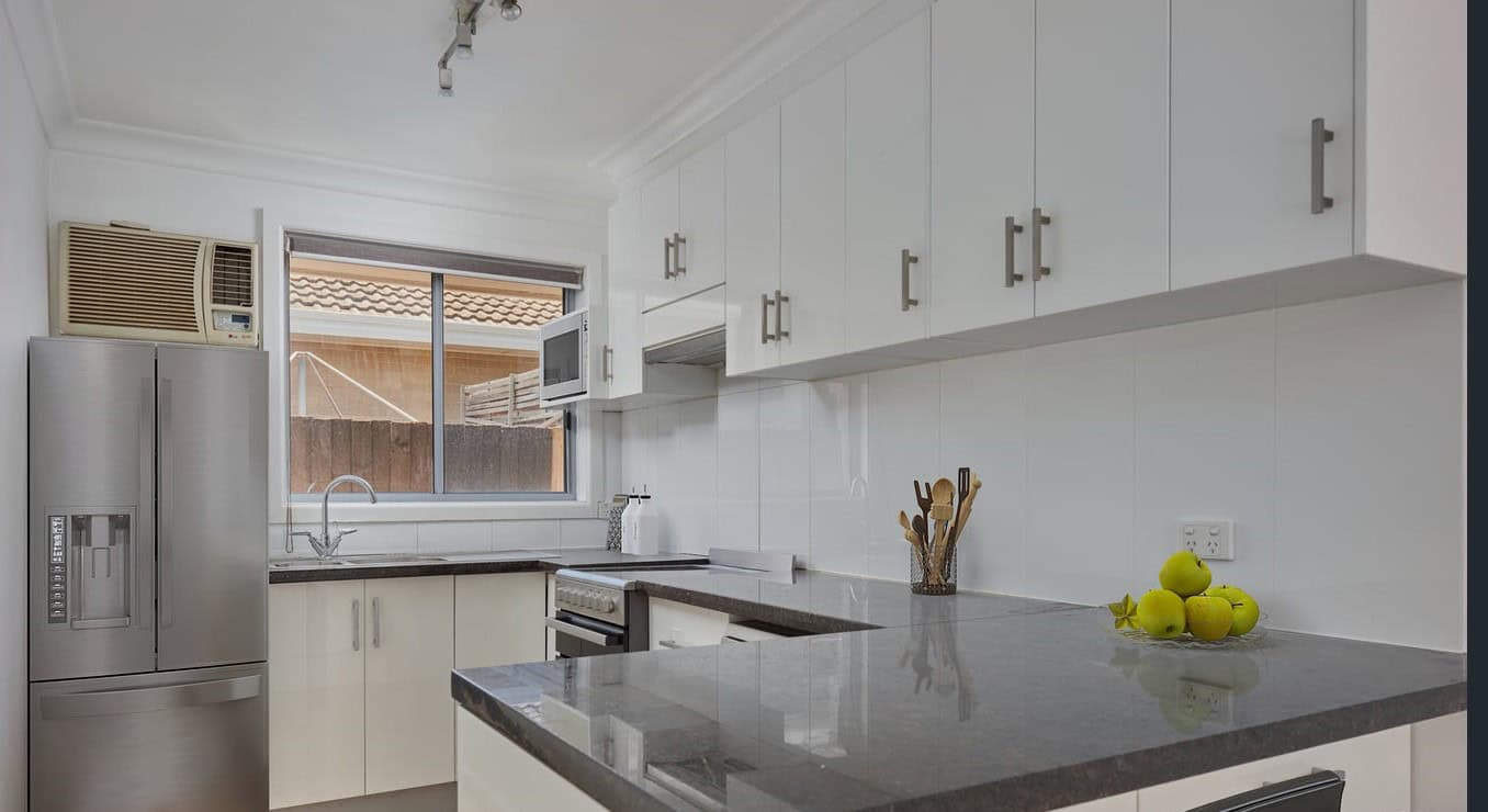 Bright modern kitchen with white cabinetry, stainless steel appliances, and a window overlooking the backyard - perfect for Australian property buyers.
