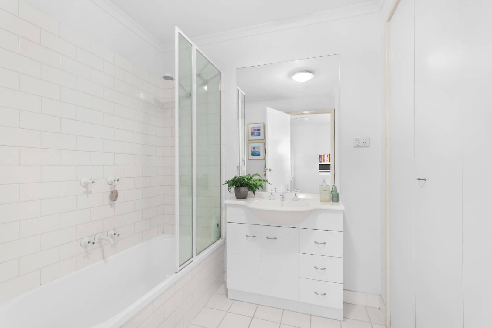 Bright modern bathroom with white tiles and fixtures, featuring a bathtub, shower, and stylish vanity—ideal for contemporary homes in Ember Estate real estate listings.