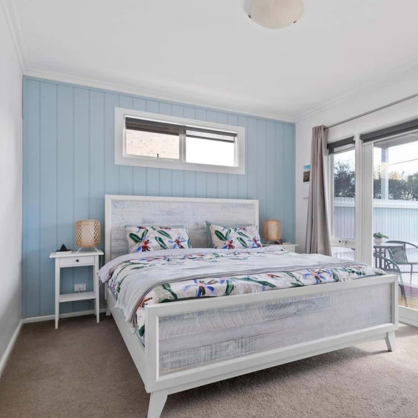 Bright coastal bedroom with a large window and balcony access, featuring a white bed and colourful bedding, perfect for a relaxed Chelsea home.