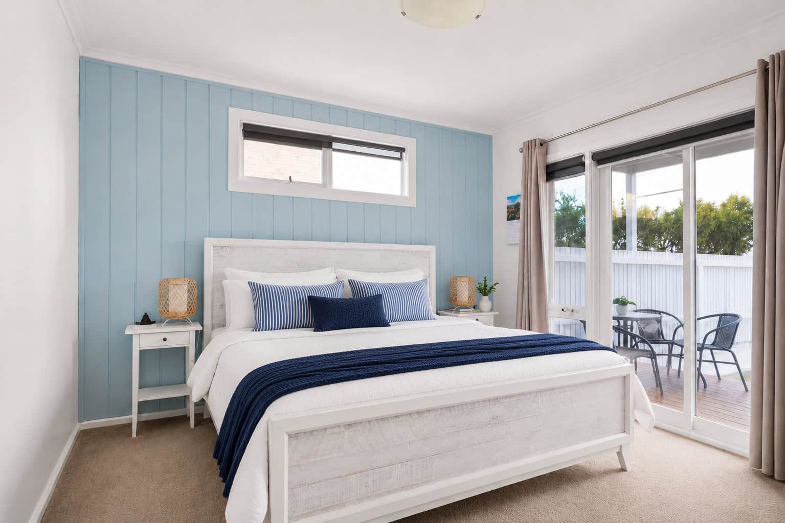 Bright and airy bedroom featuring a white bed, blue accents, and access to a balcony with outdoor seating, perfect for relaxing in Chelsea's prime location.