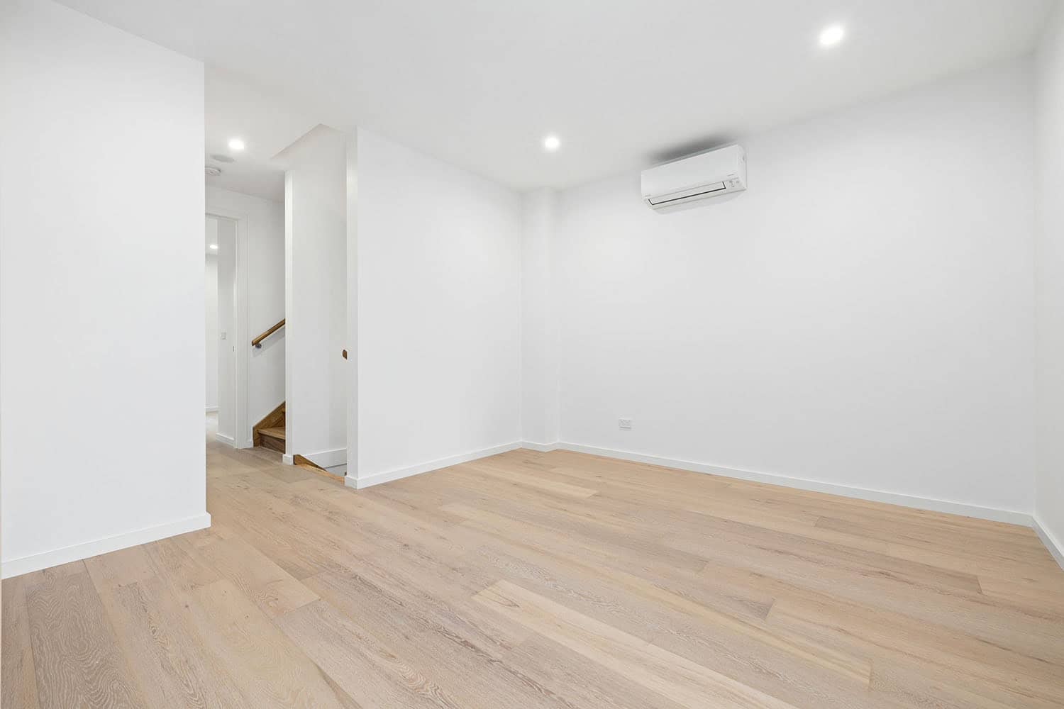 Bright and spacious living room featuring white walls, light wooden flooring, and a wall-mounted air conditioning unit, ideal for comfortable living in Ember Estate.