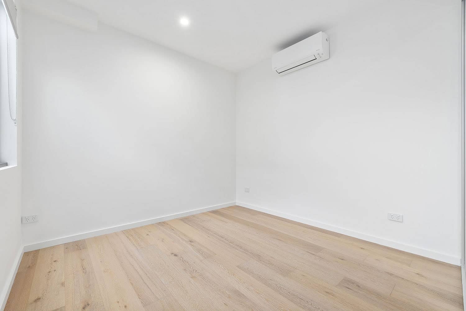 Bright, modern empty room with white walls, wooden flooring, and an air conditioning unit, ideal for property listings and real estate marketing in Australia.