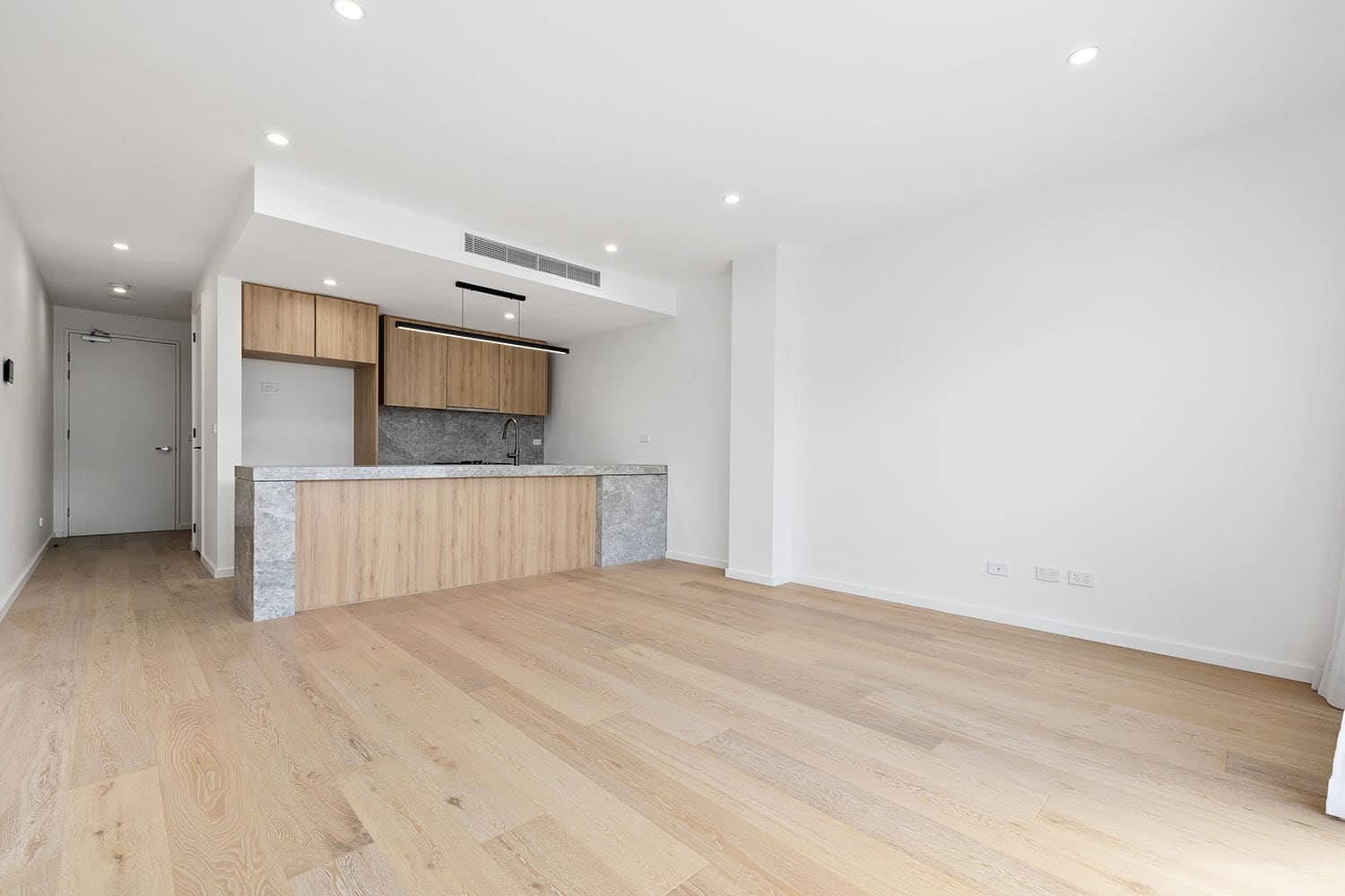 A spacious, bright open-plan living area featuring a contemporary kitchen with wooden cabinetry and a grey stone island, perfect for family living and entertaining.