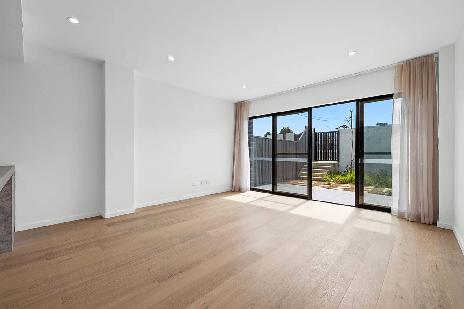 Bright and spacious living room with large glass sliding doors, wooden flooring, and neutral walls, ideal for family living and entertaining.