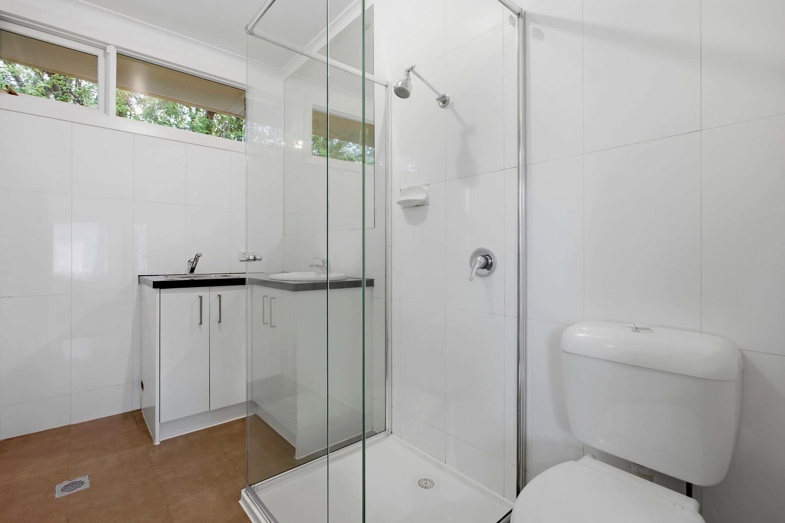 Contemporary bathroom with glass shower enclosure, white tiles, and a vanity with storage in Ember Estate property.
