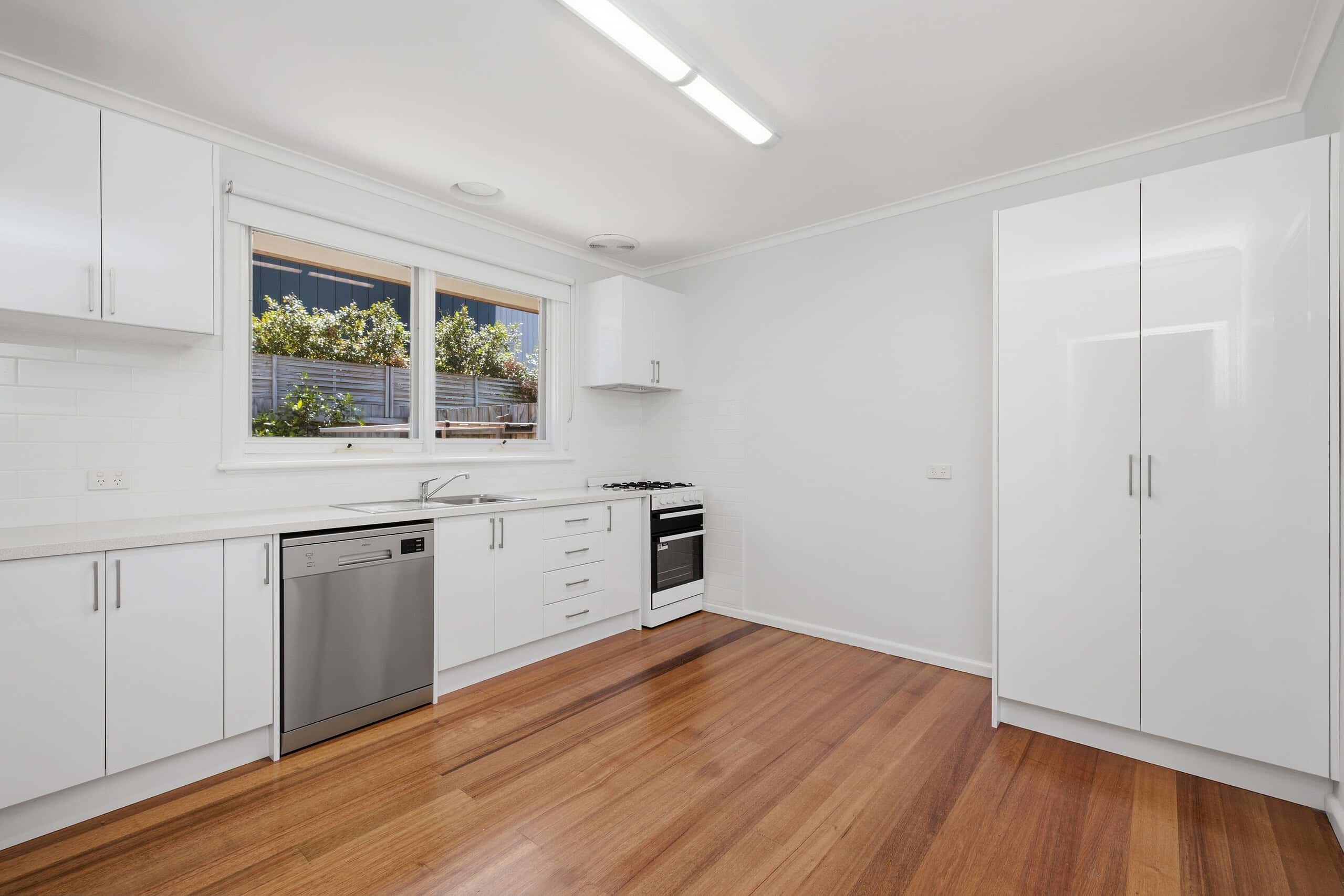 Spacious modern kitchen with white cabinetry, stainless steel appliances, and wooden flooring in a Mordialloc apartment.