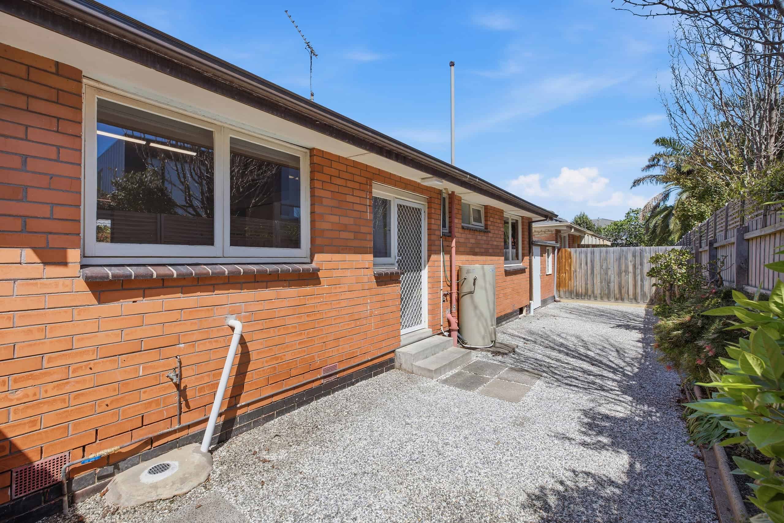 Exterior view of a brick 2-bedroom unit with a gravel driveway and garden, located near Mordialloc Beach in Melbourne.